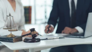 A lawyer and client intently review legal documents, with a gavel and scales of justice on the table
