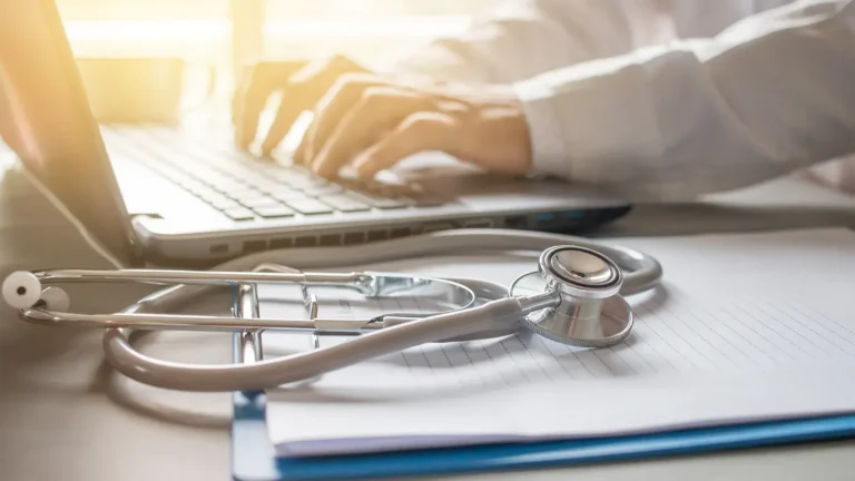 Doctor working on a Laptop with Stethoscope prescription clipboard